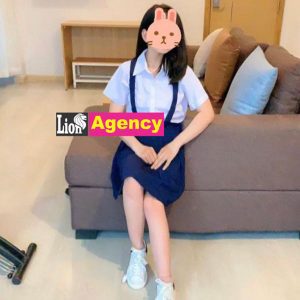 A girl in a school uniform sitting on a couch, being admired by a 707 kl escort or kuala lumpur escort.