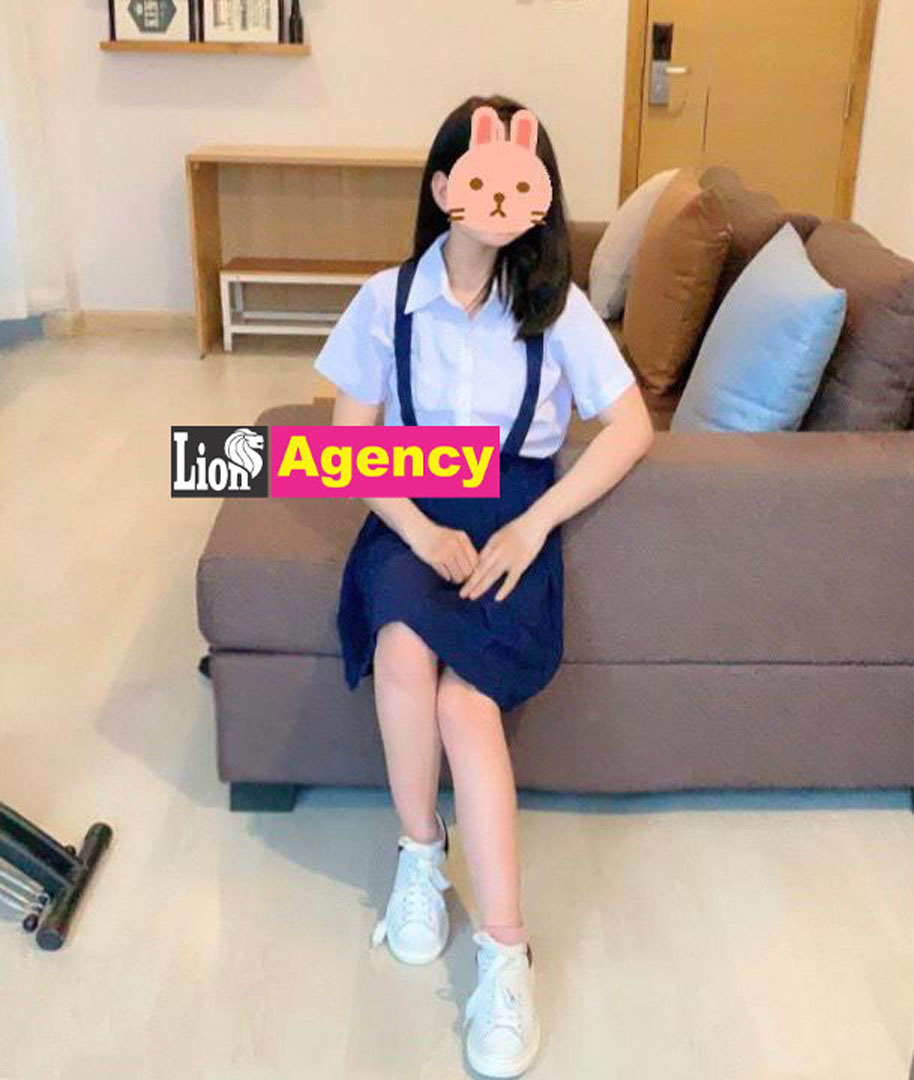 A girl in a school uniform sitting on a couch, being admired by a 707 kl escort or kuala lumpur escort.