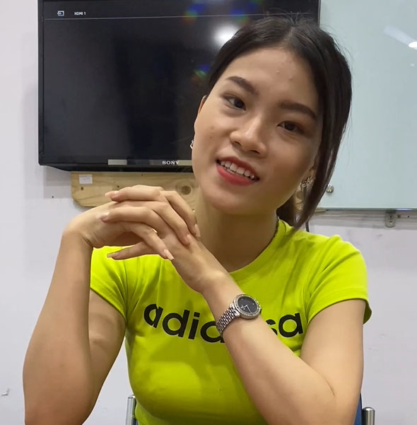A young woman in a yellow shirt sitting at a desk for KL Escort service.