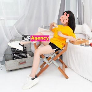 A woman in a yellow shirt sitting on a 707 bed.