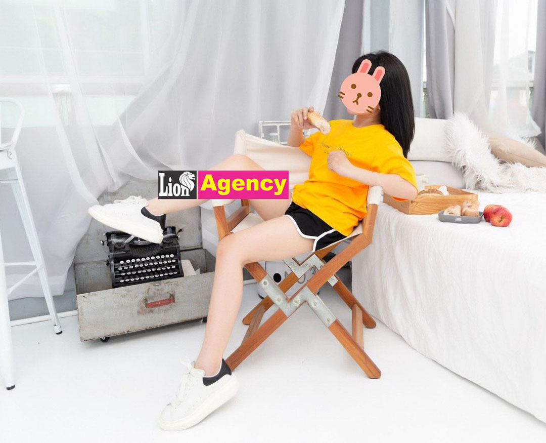 A woman in a yellow shirt sitting on a 707 bed.