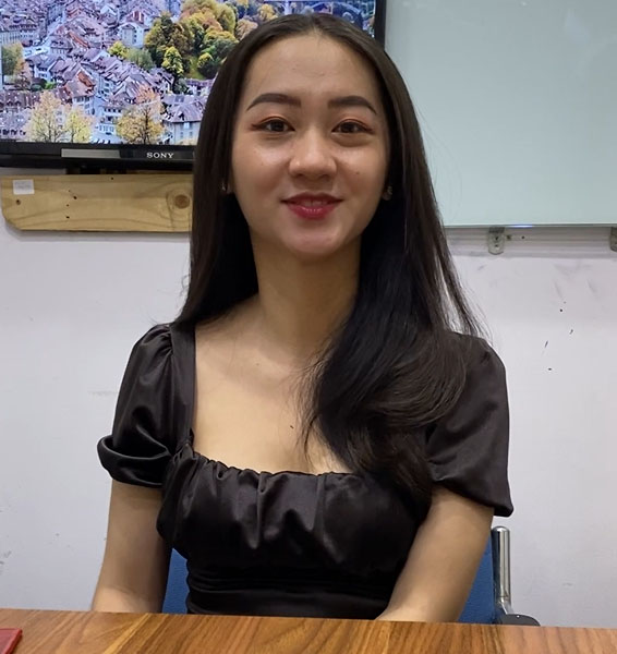 A stunning woman in a black dress sitting at a desk, exuding elegance and grace.