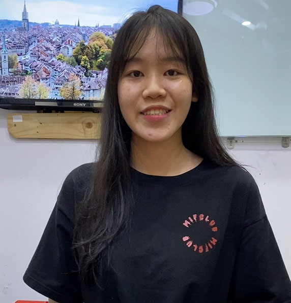 An Asian woman in a black t-shirt standing in front of a TV.